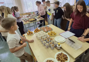 Uczniowie oglądają i kupują przekąski przy szkolnych stoiskach z potrawami.