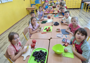 Uczniowie rozmawiają przy stoliku na temat warzyw i owoców.