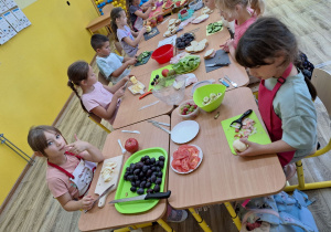 Dziewczynki i chłopcy z zaangażowaniem kroją przyniesione produkty.