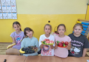 Uczennice trzymają w ręku owoce i warzywa.
