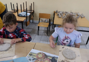 Przedszkolaki za pomocą dostępnych narzędzi dekorują swoją pracę.