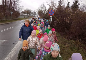 Grupa uśmiechniętych dzieci idzie chodnikiem na spacer w poszukiwaniu wiosny.