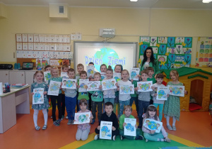 11.Zdjęcie ukazuje grupę przedszkolaków, którzy trzymają swoje ekologiczne prace. Wszyscy są ubrani w zielone barwy i znajdują się w Sali przedszkolnej.