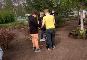 13.Zdjęcie ukazuje grupę nastoletnich chłopców na szkolnym podwórku. Chłopcy porządkują przyszkolny ogródek.