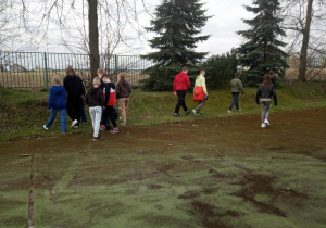 2.Zdjęcie ukazuje grupę dzieci w wieku szkolnym na boisku wśród zielonych drzew.