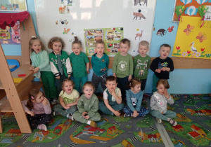 21.Zdjęcie ukazuje grupę przedszkolaków. Wszyscy są ubrani w zielone barwy i znajdują się w Sali przedszkolnej.