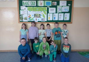 3.Na zdjęciu widzimy grupkę młodszych dzieci ubranych w zielone barwy na korytarzu szkolnym pod ekologiczną gazetką.