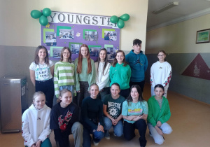 5.Na zdjęciu widać grupę uśmiechniętych nastolatków, ubranych w zielone barwy na korytarzu szkolnym
