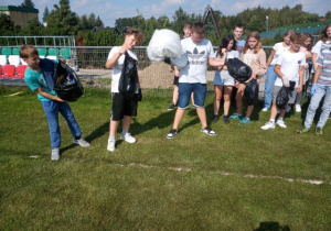 Grupa uczniów na boisku , trzymają worki na śmieci , pokazują zebrane odpady.