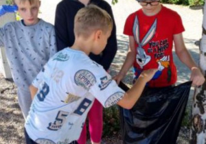 Na zdjęciu czwórka uczniów. Jeden z chłopców trzyma worek na śmieci, drugi wrzuca śmieci.