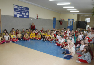Zdjęcie ukazuje dużą grupę siedziących na korytarzu dzieci