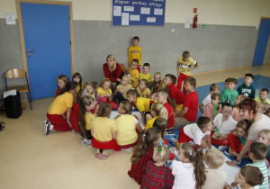 zdjęcie ukazuje grupę siedzących na korytarzu szkolnym dzieci wraz z nauczycielem, które pracują nad brystolem