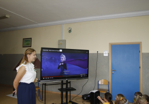 zdjęcie ukazuje nauczyciela języka angielskiego oraz tablicę multimedialną oraz grupkę dzieci