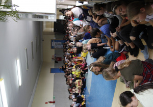 zdjęcie ukazuje grupę siedzących na korytarzu szkolnym dzieci