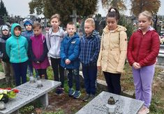 Uczniowie stojący przy grobach na cmentarzu
