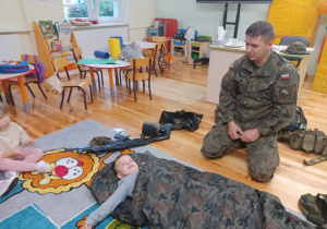 Żołnierz uczy dziecko jak korzystać ze śpiwora oraz karimaty.