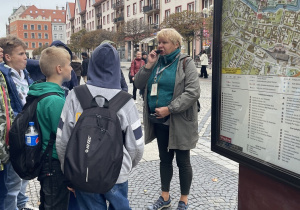 Zadowoleni uczniowie słuchają pani przewodnik i zwiedzają Wrocław.