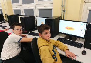 Pracownia komputerowa. Dwóch chłopców projektuje swoje imienne breloczki. Na pulpicie ekranu widoczny jest program Tinkercad i zaprojektowane w nim modele.