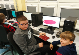 Pracownia komputerowa. Dwóch chłopców projektuje swoje imienne breloczki. Zaprojektowane modele widoczne są na pulpicie ekranu.