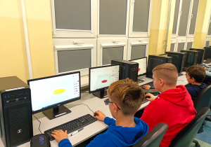 Pracownia komputerowa. Trzech chłopców projektuje swoje imienne breloczki. Zaprojektowane modele widoczne są na pulpicie ekranu.