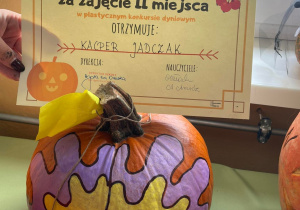 zdjęcie ukazuje kolorową dynię konkursową oraz dyplom