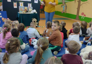Kobieta w żółtej bluzce pokazuje opowiada dzieciom o misiach.
