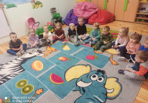 Dzieci trzyletnie siedzą w kole na kolorowym dywanie.
