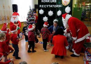 Mikołaj wręcza dzieciom z grupy Biedronki prezenty a Pan Wójt częstuje przedszkolaki cukierkami