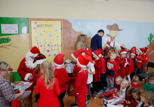 Mikołaj wręcza dzieciom z grupy Krasnoludki prezenty a pan wójt częstuje cukierkami.