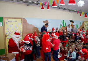 Mikołaj wręcza dzieciom z grupy Pszczółki prezenty a pan wójt częstuje cukierkami.