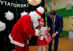 Mikołaj wręcza wyróżnienie i nagrodę dziewczynce podczas Mikołajkowego Konkursu Recytatorskiego