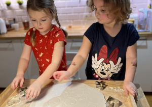Dwie dziewczynki wykrawają foremkami od pierników ozdoby z ciasta.