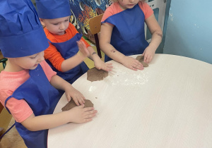 Dzieci przedszkolne uklepują placki z kawałków ciasta na pierniki.