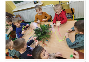 Przedszkolaki za pomocą różnych ozdób zdobią stroiki świąteczne.