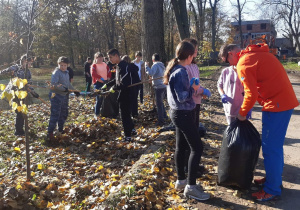 trzy uczennice pomagają nauczycielowi pakować liście do worka