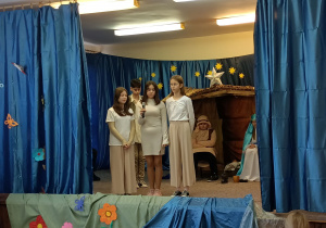 Grupa uczniów stojących na scenie. W tle widać szopkę w której siedzi Józef i Maryja.