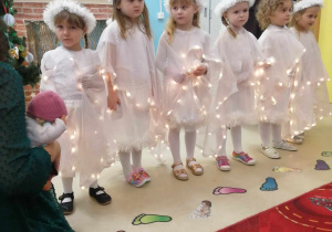 Dziewczynki ubrane na biało stoją w rzędzie.