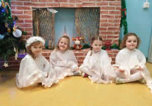 Cztery dziewczynki ubrane na biało przy kominku.