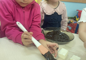Dziewczynka smaruje białą piankę polewą czekoladową.
