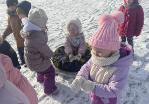 Dzieci w zimowych strojach ciągną ponton po śniegu