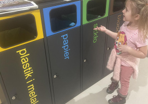 Dziewczynka przy pojemnikach do segregacji śmieci.