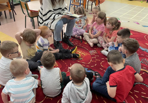 Dzieci siedzą na dywanie i słuchają czytanej bajki.