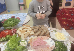 Chłopiec w szarym dresie wybiera produkty na zdrową kanapkę.