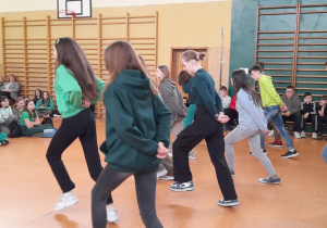 zdjęcie ukazuje grupę tańczących dziewcząt, które prezentują taniec irlandzki przed uczniami szkoły w Sali gimnastycznej