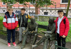 Rajmund, Wojtek i Bartek z rzeźbami na ławce przed seminarium duchownym w Krakowie