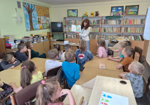 Dzieci z zainteresowaniem słuchają czytanych legend przez panią z biblioteki.