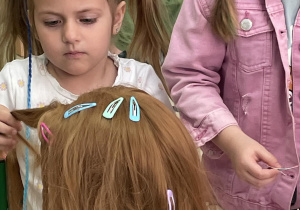 Dziewczynki przypinają spinki na główce fryzjerskiej.
