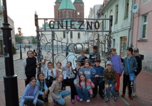 grupa uczniów na ławeczce z napisem Gniezno na tle Katedry Gnieźnieńskiej