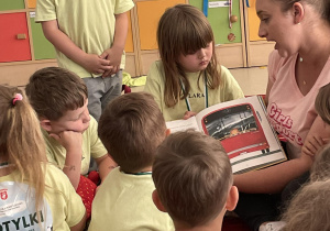 Dzieci przedszkolne w limonowych imiennych koszulkach oglądają obrazki w książce