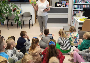 Pani Grażyna pokazuje dzieciom książki , jakie znajdują się w bibliotece i które można wypożyczyć.